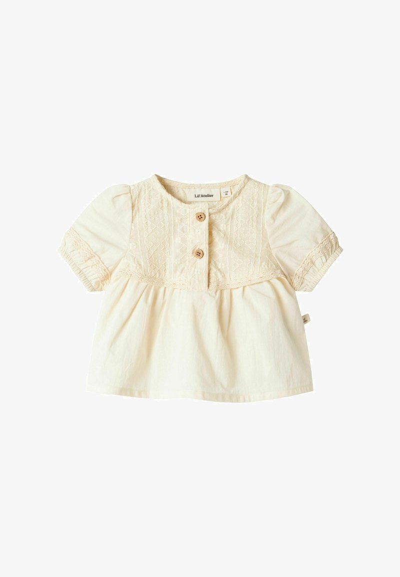 Kremfarget bomullstopp med korte puffermer, med knappeåpning foran og blondedetaljer langs yoke og midje.