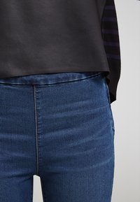 Camiseta negra con rayas moradas en las mangas, combinada con jeans de denim azul oscuro con una textura suave y un diseño ajustado.