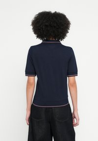 Tengerészkék póló, testhezálló kialakítással, rövid ujjal, és kontrasztos szegéllyel a galléron és az ujjakon. Sima textúrájú és laza stílusú.