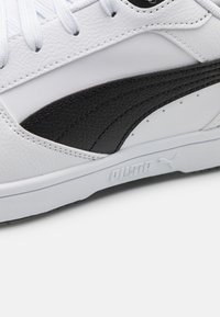 Hvit skinnsneaker med en svart teksturert sidepanel, med hvite snører og en gummi såle. Logo preget på siden.