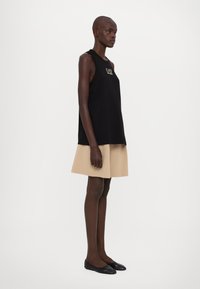 Melnas bezpalvīgas augšdaļas ar logotipu, apvienotas ar bēšas krāsas plati izpletna svārkiem. Modelim kājās melnas baleta kurpes. Gluda tekstūra, brīvs piegriezums.