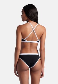 Svart bikiniuppsättning med vit trim; har en korskonstruktion på toppen, högmidjade byxor och en mjuk textur.
