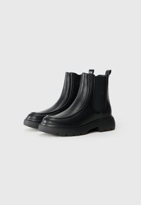 Botas de tobillo de cuero negro con paneles laterales elásticos, textura suave, punta redondeada, suela gruesa y tiradores para ponerlas y quitarlas con facilidad.