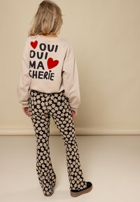 Beige sweatshirt met zwarte en rode tekst op de achterkant, gecombineerd met uitlopende zwarte broek met een crèmekleurig bloemenpatroon. Zwarte platform schoenen.