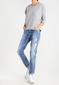 Maglietta grigia a maniche lunghe, jeans chiari strappati e scuciti, e sneakers bianche. Outfits casual con vestibilità comoda e texture morbida.