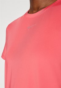 Camisa de manga corta y cuello redondo en tejido rosa vibrante. Presenta un discreto logo de Nike en gris en el pecho. Textura suave, ajuste atlético.
