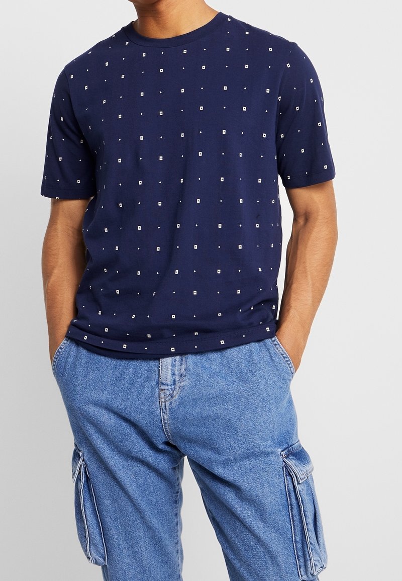 Navy-blue cotton t-shirt with a crew neck, featuring a geometric pattern of white squares and dots. Short sleeves and relaxed fit.