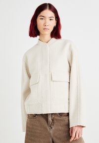 Beige uldblandingsjakke med mandarinkrave, frontknaplukning, to store påsatte lommer og struktureret stof. Afslappet pasform.
