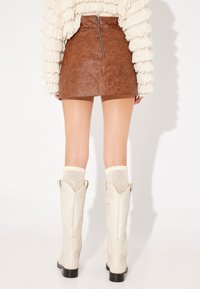 Minigonna in finta pelle marrone con zip sul retro. Abbinata a stivali cowboy bianchi alti fino al ginocchio e calzini a coste color crema.