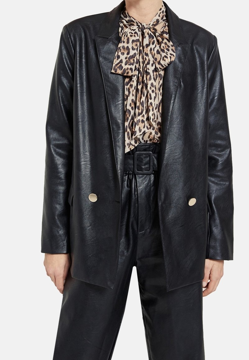 Blazer en similicuir noir présentant un design classique, avec des revers crantés, deux boutons dorés et une finition texturée. Associé à une écharpe imprimée léopard.