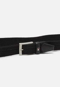 Schwarzer, gewebter Gürtel aus elastischem Material. Verfügt über eine silberne Metallschließe und schwarze Lederakzente mit einem kleinen Logodetail.