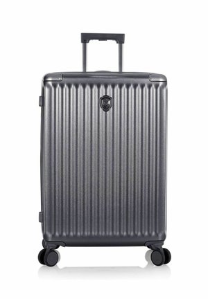 Valise rigide gris foncé avec des rainures verticales, quatre roues pivotantes et une poignée télescopique étendue.