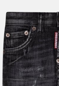 Sorte denimjeans med fem lommer, kobbernitter og et rødt logo mærke på baglommen; falmet tekstur med synlige sømme.