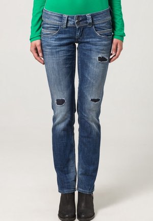 Jean skinny bleu avec des patches déchirés, fermeture à deux boutons et décoloration légère. Le matériau semble être du denim avec une texture lisse.