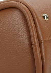 Primo piano di una borsa in pelle marrone, con una superficie texture, bordi arrotondati e accessori in tonalità oro.