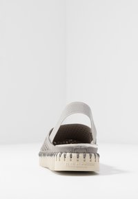 Scarpa grigia perforata con una soffice fascia posteriore elastica e una suola crema texturizzata con dettagli in gomma e marchio sul tallone.
