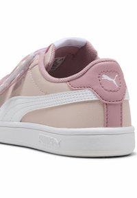 Baskets Puma avec un design rose pâle et blanc, en matériau cuir synthétique, forme arrondie, accents texturés et détail du logo sur le talon.