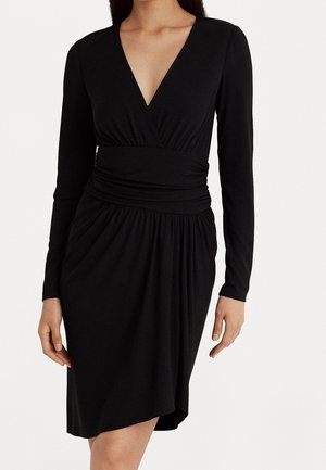 Robe noire avec un décolleté en V profond, manches longues, taille froncée et jupe plissée. Confectionnée en tissu lisse et extensible pour le confort et une bonne tenue.