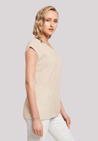 Beige t-shirt with a v-neckline and short sleeves, made of soft fabric; paired with white pants. Plain design, no visible patterns or accents.