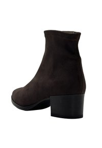 Botín de ante marrón oscuro con tacón bajo apilado y punta redondeada, mostrado desde un ángulo lateral trasero sobre un fondo blanco.