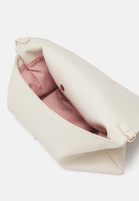 Crème gekleurde lederen tas met een zachte roze stoffen voering, voorzien van een gouden drukknoopsluiting en een platte vorm. Geopend voor interieurzichtbaarheid.