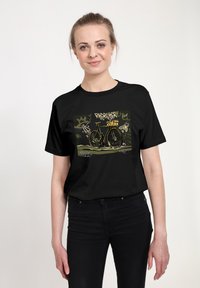 Žena v čern�ém tričku s grafikou kola a graffiti stylovými nápisy na městském pozadí.