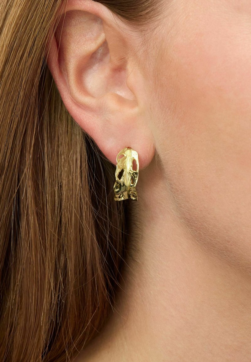 Gold-tone metal hoop earrings displaying an abstract design with cut-out sections, featuring a polished texture and irregular shape.