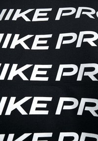 Zwart materiaal met herhaaldelijk grote witte tekst die "NIKE PRO" leest. De letters hebben een vet, modern lettertype.