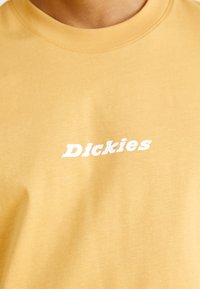 Tricou din bumbac galben, cu gât rotund, având imprimat central un logo alb "Dickies". Textură netedă, croi lejer.