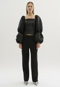 Zwarte cropped top met pofmouwen, gestructureerde stof, verticale strepen; gecombineerd met zwarte skinny trousers en spitse metallic schoenen.