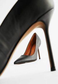 Scarpa nera in pelle con tacco alto e punta affusolata, caratterizzata da un design elegante, sottile tacco a stiletto e un interno color tan a contrasto.