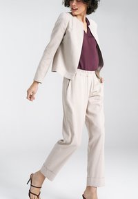 Jasno beżowa, dopasowana marynarka o skróconym kroju, zestawiona z dopasowanymi, luźnymi spodniami. Bordowa bluzka pod spodem. Sandały na obcasie.