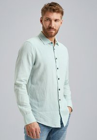Helles mintgrünes Hemd mit langen Ärmeln, schwarzen Knöpfen und einem klassischen Kragen; verfügt über einen leicht strukturierten Stoff.