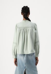 Lys grønne, langermede skjorte med rynket bryst, smockede detaljer på ermene og knappelukking, brukt sammen med et denimskjørt.