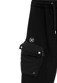 Pantalones de chándal negros con cinturilla elástica, que cuentan con un bolsillo cargo lateral con cierres a presión y cremallera, y una etiqueta de logo redonda.