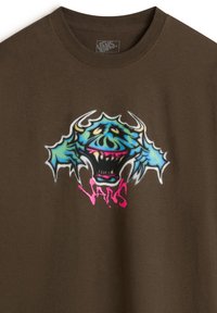 Camiseta de algodón marrón con un gráfico vibrante de un monstruo multicolor, con una gran cabeza y colmillos. Logo de "Vans" en color rosa.