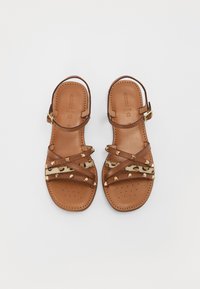 Bruna läder sandaler med korsetträmmar, guldfärgade nitar och en leopardsmönstrad accent. Platt sula med perforerad detalj ochankelspänne.