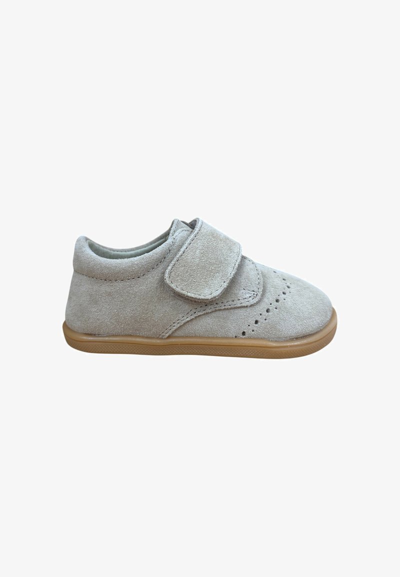 Zapato infantil de ante en gris claro, con una cinta de velcro, detalles perforados en la puntera y una suela de goma flexible beige.