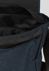 Borsa a tracolla blu in tessuto con una tasca interna foderata in rete e apertura superiore. Texture morbida con dettagli neri e tracolla regolabile.