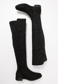 Bottes noires au-dessus du genou avec une finition en daim et des panneaux en tissu extensible. Dotées d'une fermeture éclair sur le côté et d'un petit talon bloc. Texture lisse.