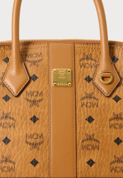 Sac à main MCM en cuir fauve avec deux anses, plaque logo dorée, monogramme imprimé et motifs de losanges noirs sur surface texturée.