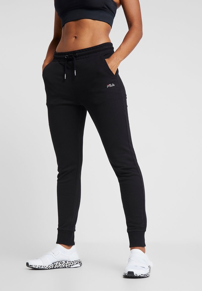 Pantalons de jogging noirs avec une taille élastique à cordon de serrage et des poches latérales. Décorés d'un logo rouge sur la hanche. Associés à des chaussures blanches avec une semelle à imprimé léopard.