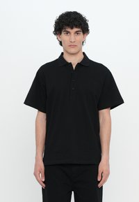 Svart kortermet polo skjorte med teksturert stoff, klassisk krage og fire knapper foran, brukt med matchende svarte bukser.