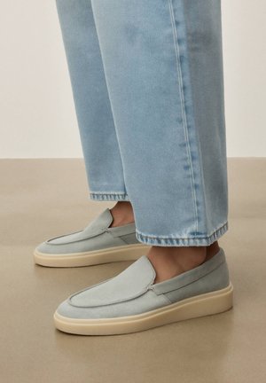 Baskets bleu clair à enfiler avec semelles beiges portées avec un jean droit bleu clair sur un sol neutre.