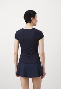 Ναυτικό αθλητικό τοπ με κοντά μανίκια, εφαρμοστό σχέδιο, υφή υφάσματος και στρογγυλή λαιμόκοψη, συνδυασμένο με φούστάκι ναυτικού χρώματος σε άνοιγμα.