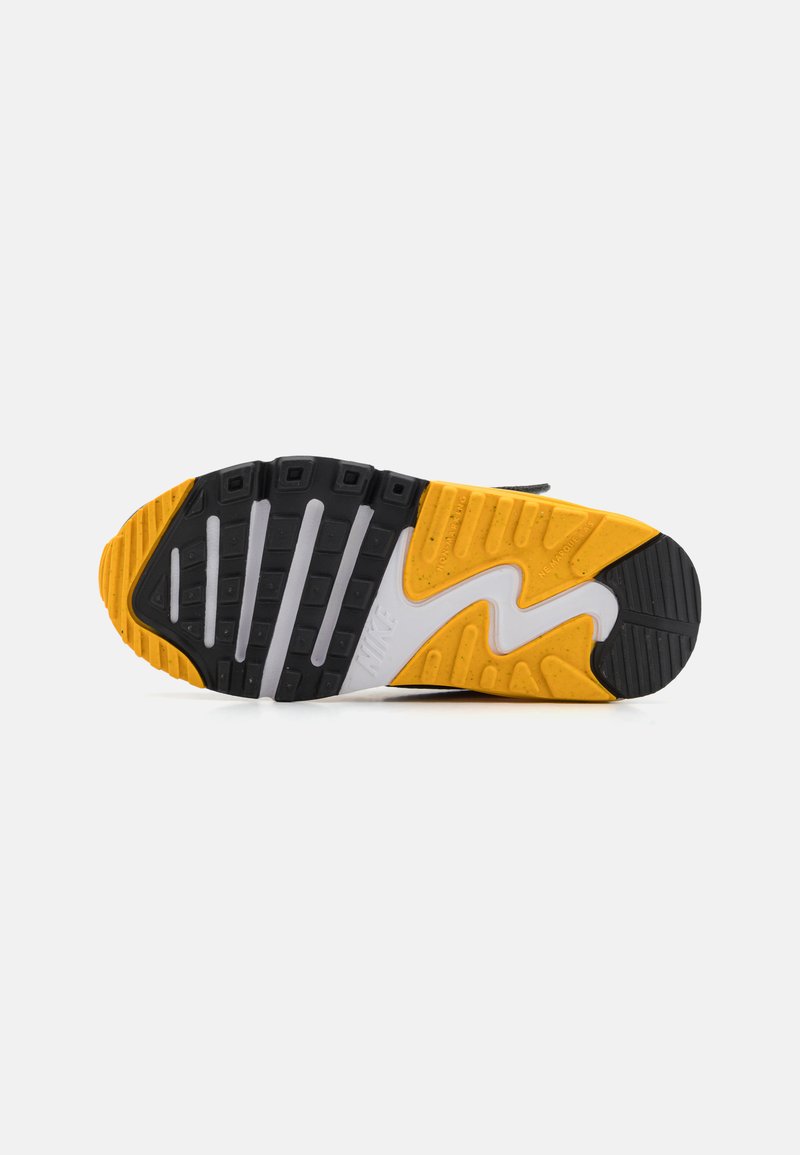 Suela de zapatilla Nike con un diseño de goma en negro, blanco y amarillo. Ranuras prominentes y un patrón de olas mejoran la adherencia y el estilo.
