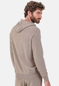 Sweat à capuche marron en maille avec une finition texturée, des poignets et un ourlet côtelés, une capuche à cordon de serrage, avec une coupe décontractée et des variations subtiles de couleur.