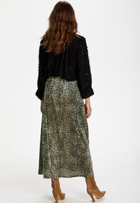 Černý texturovaný top s dlouhým rukávem v kombinaci s dlouhou zeleno-béžovou sukní s leopardím vzorem, nošený s béžovými botami na podpatku.