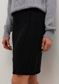 Črna pletena svinčnik krila z motnikom in teksturirano površino, v kombinaciji s svetlo sivo pleteno sv sweaterjem.