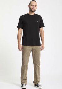 T-shirt nera in cotone con maniche corte, collo rotondo e piccolo logo sul petto. Abbinata a pantaloni kaki e sneakers nere e bianche.